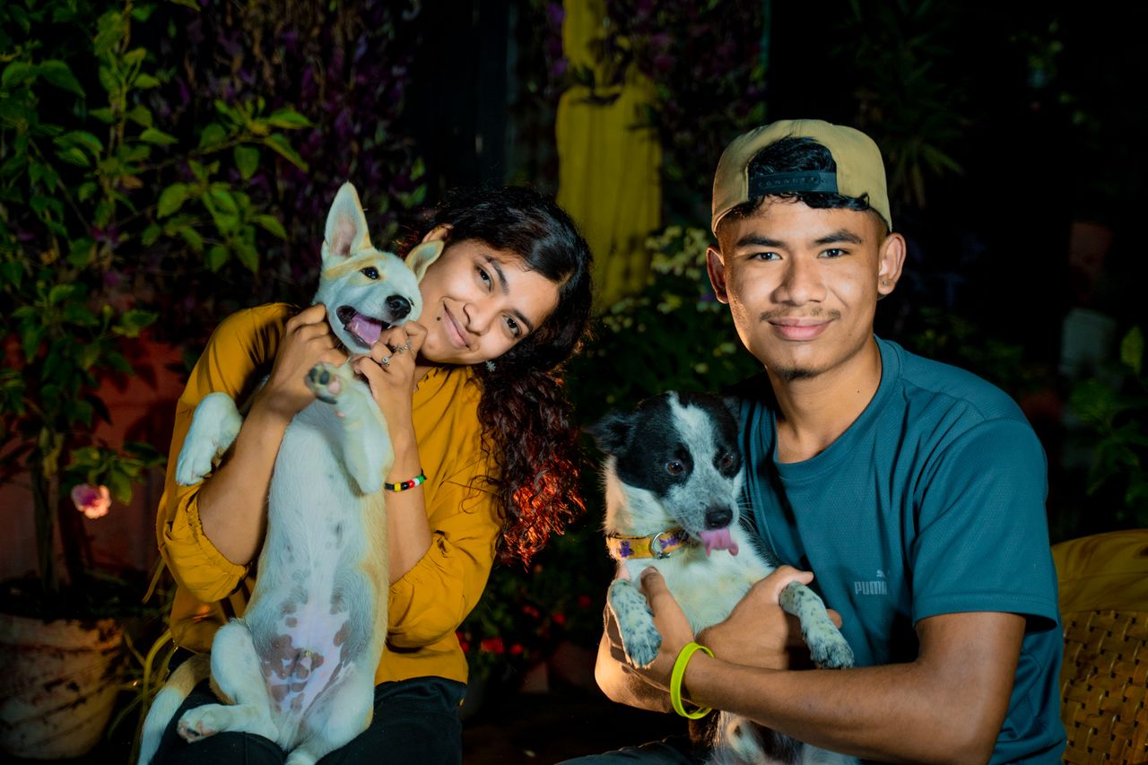 gallery-06 Young couple posing with their smiling dogs in an outdoor setting.
